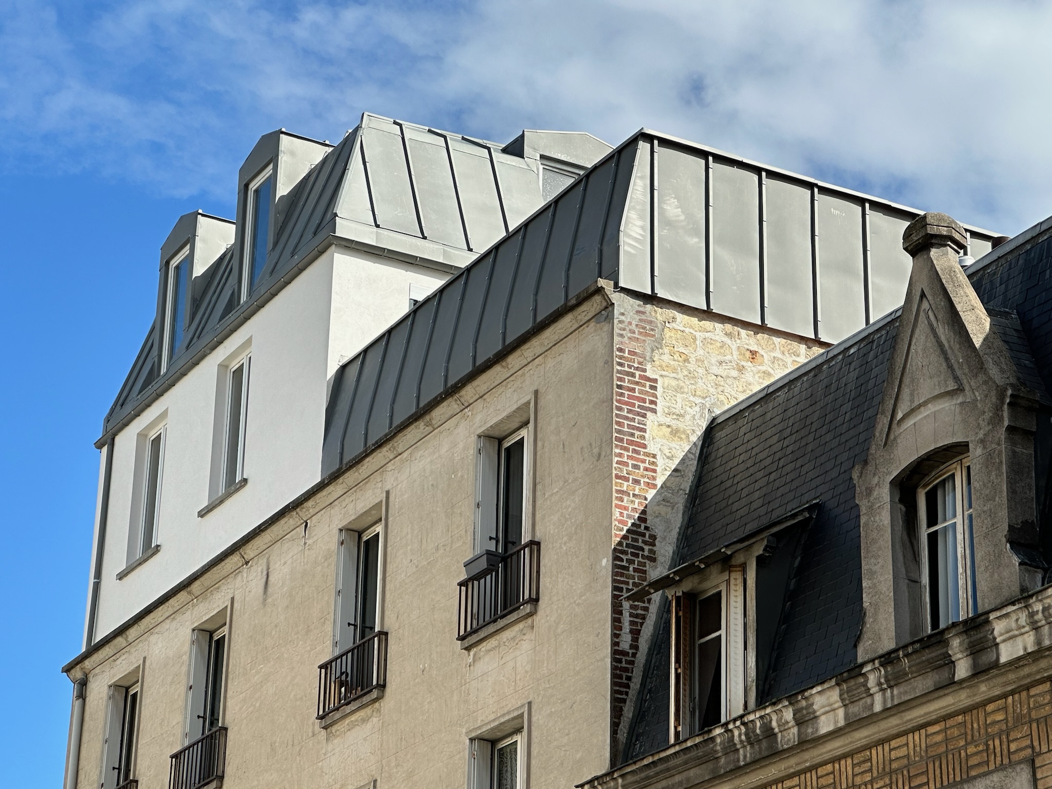 Façade d’un immeuble parisien avec surélévation en ossature métallique légère recouverte de zinc, nouveaux étages modernes au-dessus d’une construction traditionnelle.